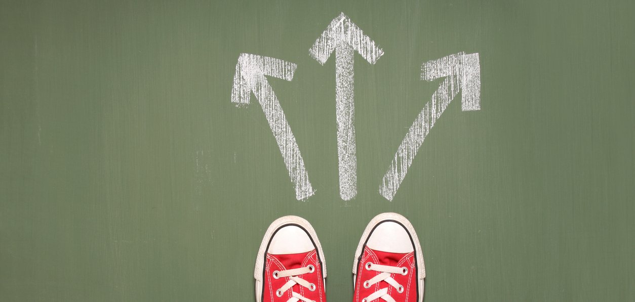 Füße einer Person stehen vor drei Pfeilen, die in unterschiedliche Richtungen zeigen.
