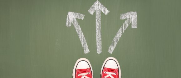 Füße einer Person stehen vor drei Pfeilen, die in unterschiedliche Richtungen zeigen.