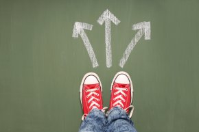 Taking decisions Füße einer Person stehen vor drei Pfeilen, die in unterschiedliche Richtungen zeigen.