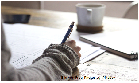 Unterarm einer Person mit Stift in der Hand und Papieren.