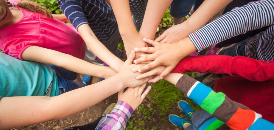 Kinder, die im Kreis stehen und in der Mitte ihre Hände zusammenführen