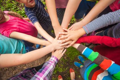 Kinder, die im Kreis stehen und in der Mitte ihre Hände zusammenführen