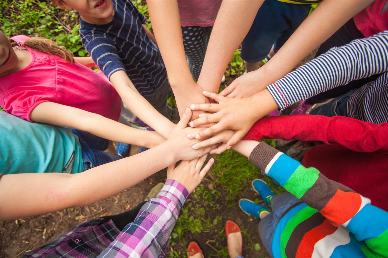 Kinder, die im Kreis stehen und in der Mitte ihre Hände zusammenführen