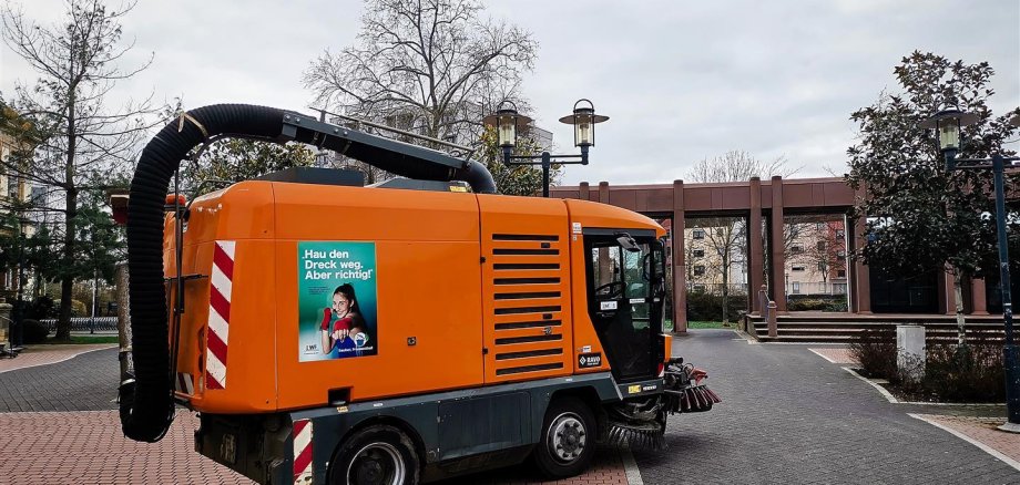 Eine Kehrmaschine mit Saugvorrichtung auf dem Mina Karcher-Platz mit Anti-Littering-Plakat