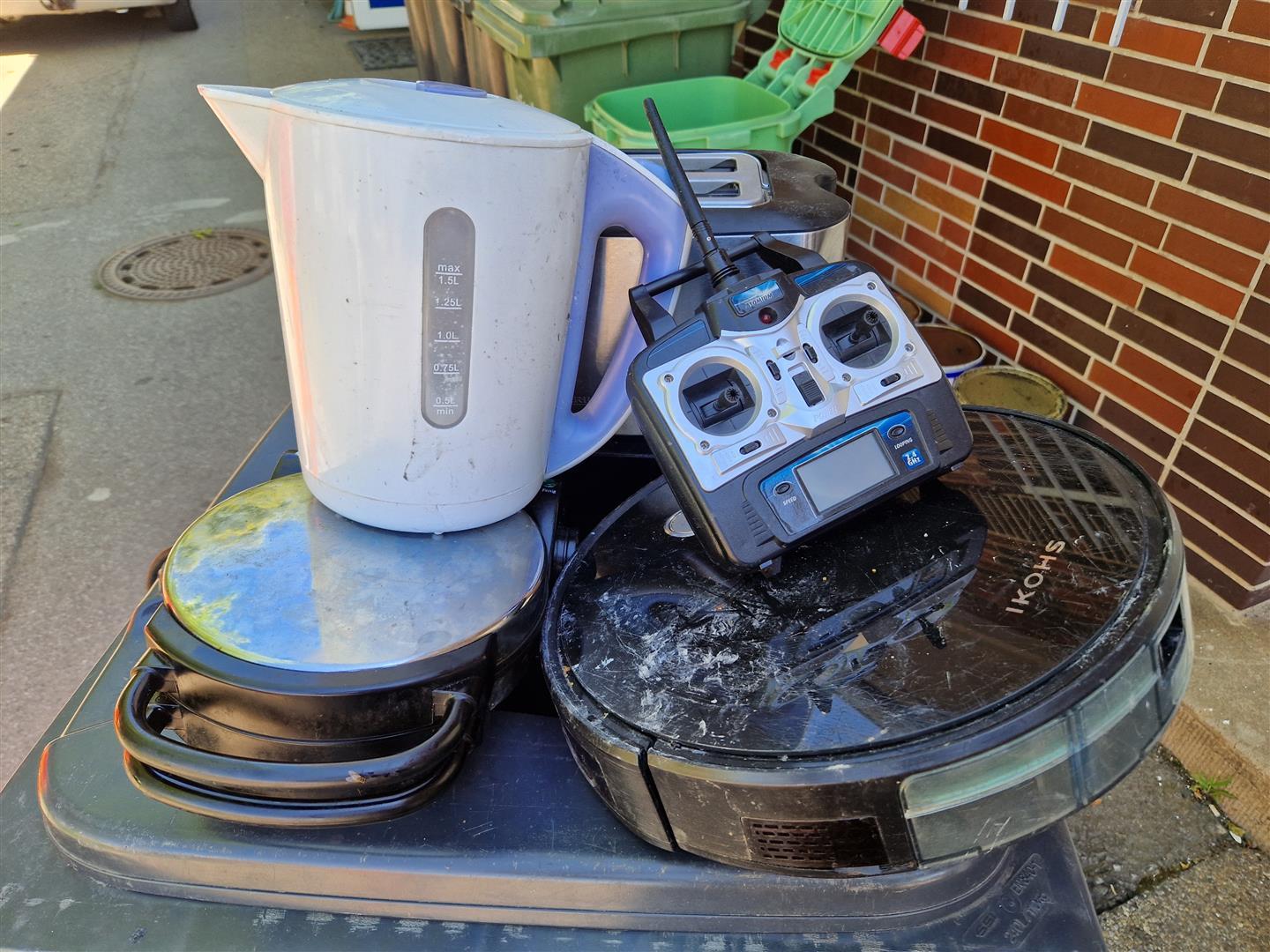 Verschiedene kleine Elektrogeräte auf einer Mülltonne angeordnet