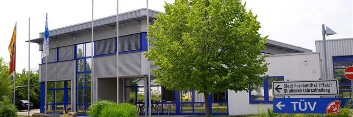 Gebäude mit Bäumen daneben. Text im Bild: TÜV