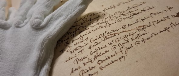 Nahaufnahme eines Eintrags im Kirchenbuch der niederländisch reformierten Gemeinde von 1591, beiliegend ein Baumwollhandschuh
