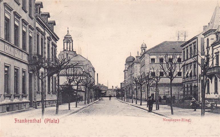 Eine historische Straßenansicht mit einer breiten, geraden Straße, gesäumt von mehrstöckigen Gebäuden auf beiden Seiten. Entlang der Gehwege stehen in regelmäßigen Abständen beschnittene, blattlose Bäume. Auf der Straße und den Gehwegen sind vereinzelt Personen zu sehen. Im Hintergrund befinden sich Gebäude mit Kuppeln und einem Turm. Am unteren Rand des Bildes steht der Schriftzug „Frankenthal (Pfalz)“ sowie „Neumayer-Ring“.