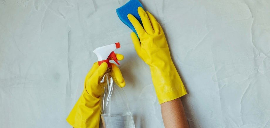 Grundreinigung Gelbe Reinigungshandschuhe, die einen Schwamm und ein Putzmittel zeigen