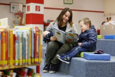 Vorlesen für die Kleinsten Eine Mutter mit Baby auf dem Arm schaut sich mit ihrem Kind ein Bilderbuch an.