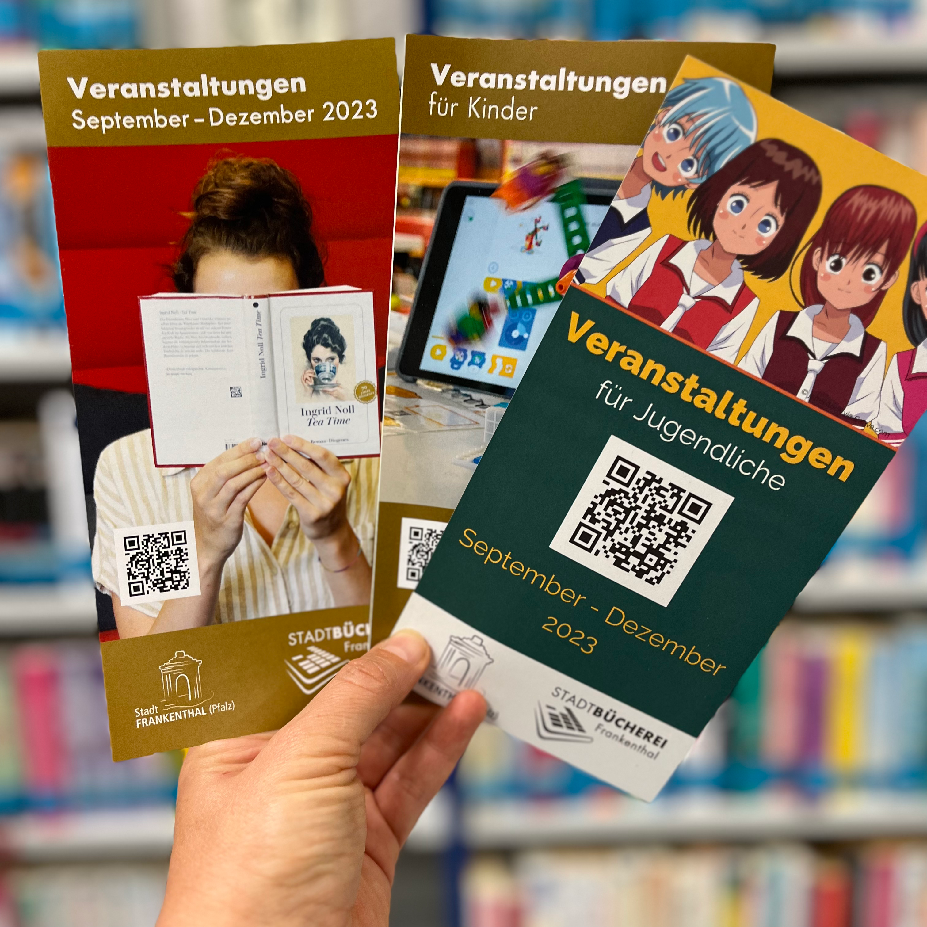 Eine Hand hält die drei neuen Veranstaltungsprogramme der Stadtbücherei