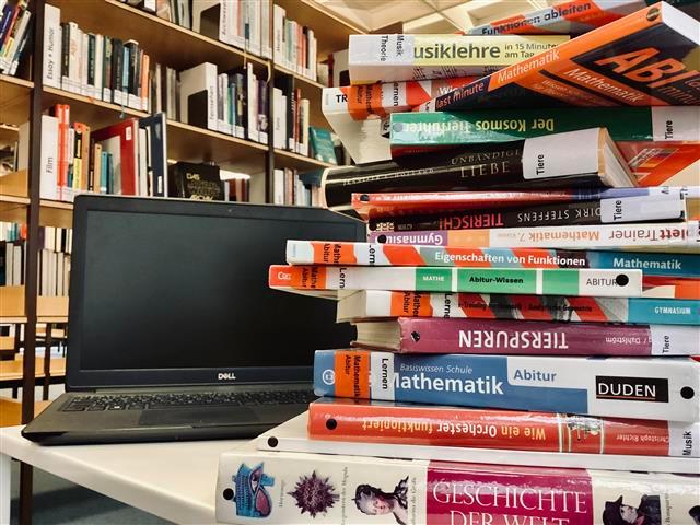 Referate SOS Im Vordergrund ist ein Stapel mit Büchern. Hinter dem Bücherstapel ist ein Laptop und in Hintergrund ist ein Bücherregal zu sehen.