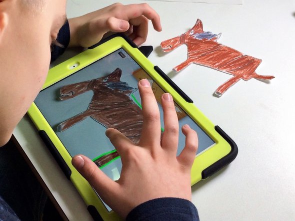 Selbst gemalte Bilder werden am Tablet vertont. Ein Kind bearbeitet am Tablet ein selbstgemaltes Bild.