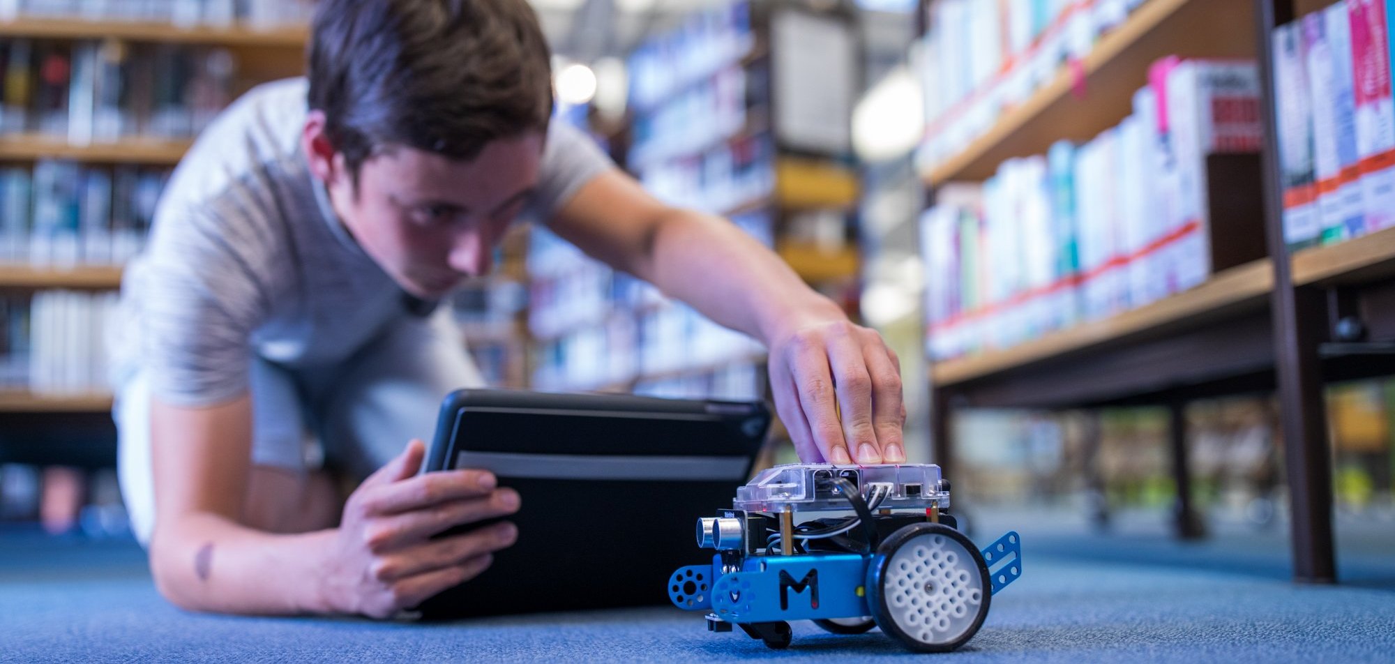 Ein Jugendlicher programmiert den Lernroboter mBot mit einem Tablet.