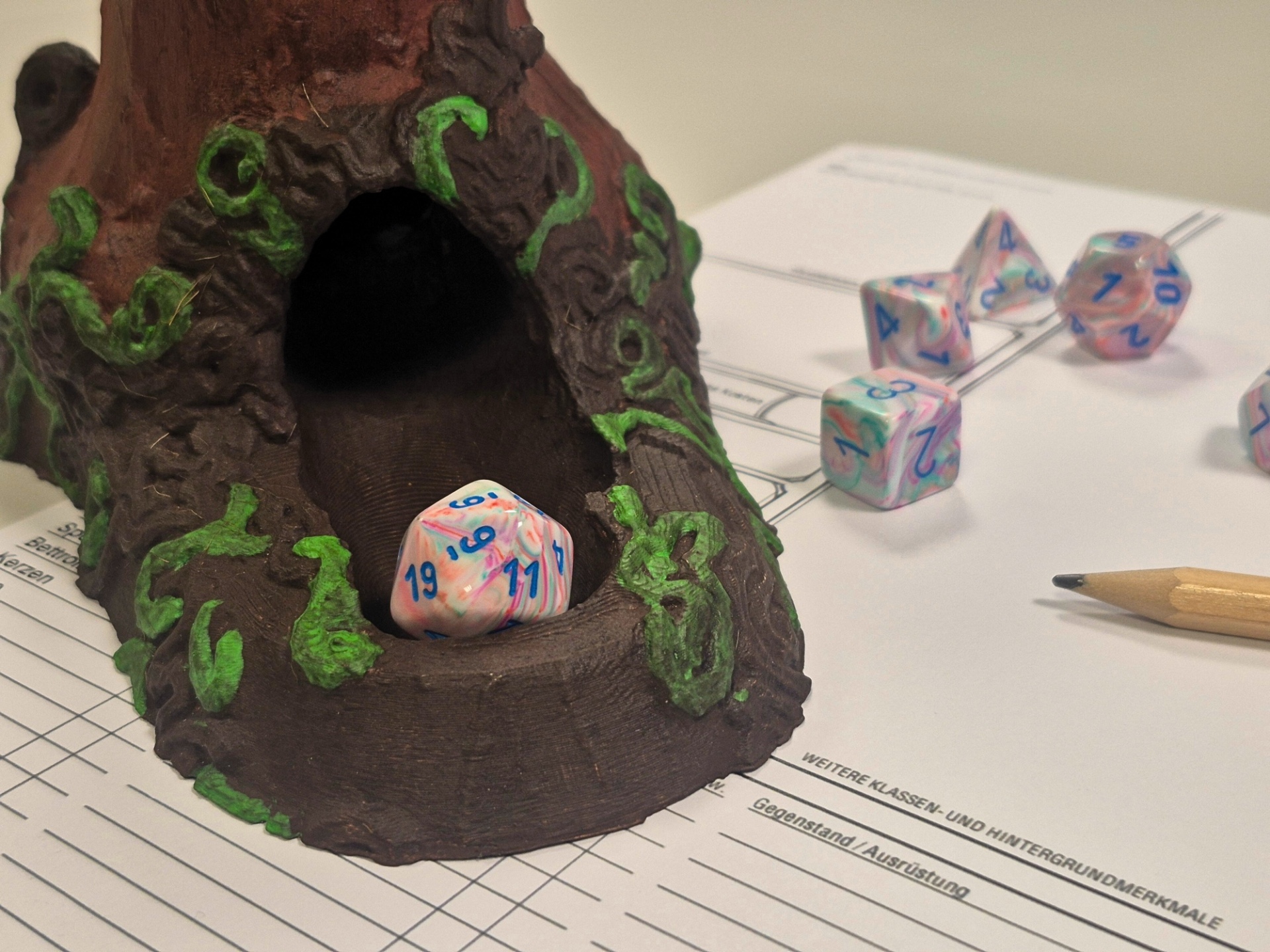 Ein Würfelturm in Form eines Baumstumpfes mit Würfeln, Stift und Papier daneben.