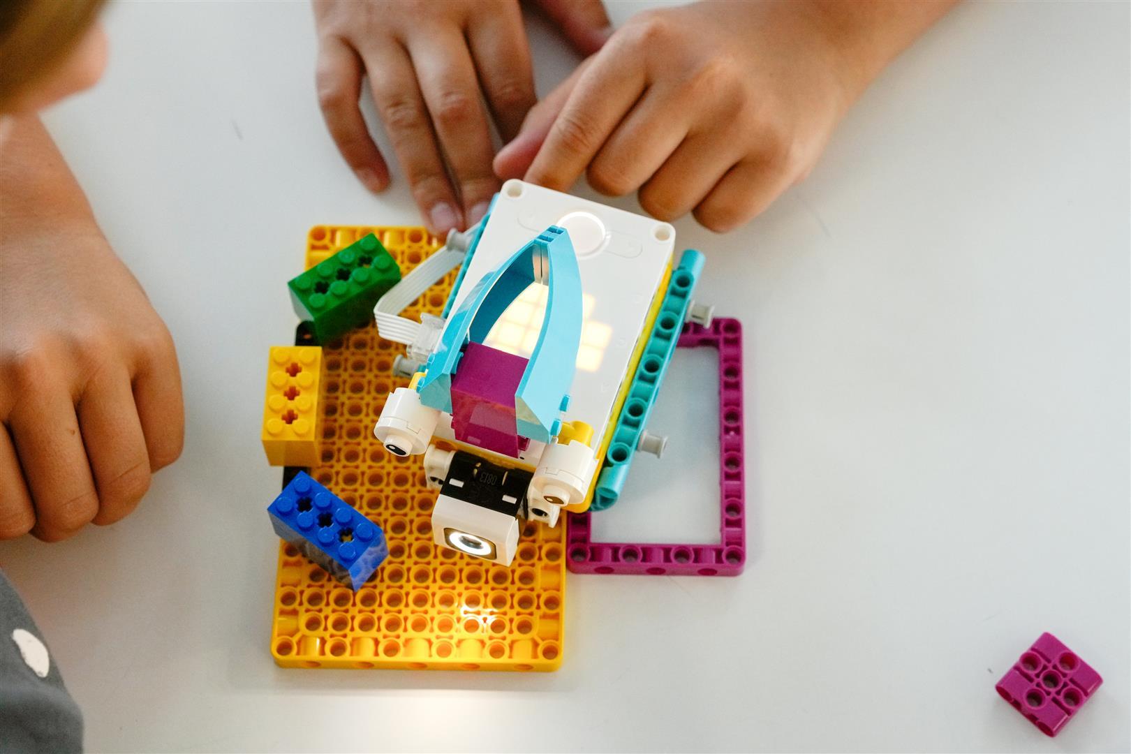 Auf einem Tisch sind Kinderhände die einen selbstgebauten Roboter bedienen