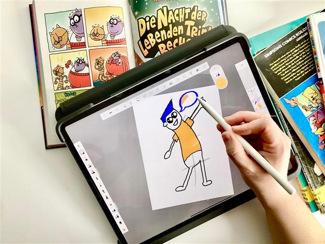 Comic-Workshop Im Hintergrund ist ein aufgeschlagener Comic. Auf dem Comic liegt ein Tablet das eine gezeichnete Comicszene zeigt.