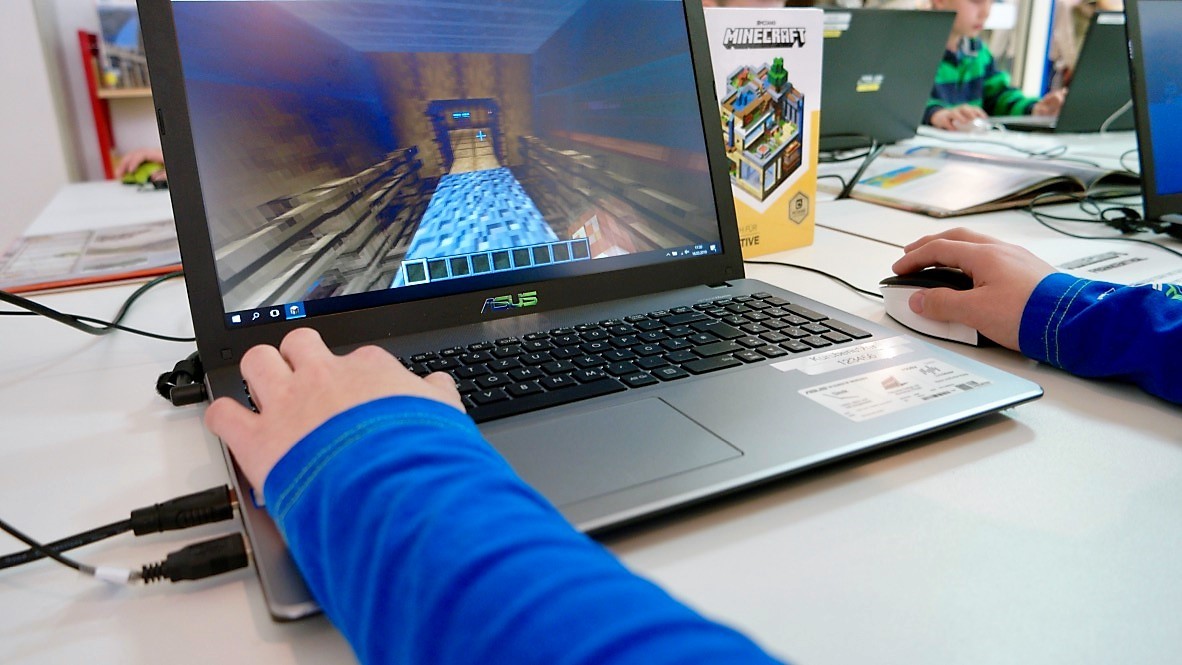 Wir craften uns ein Dorf. Minecraft Workshop Frontaler Blick auf einen Laptopbildschirm. Kinderhände bedienen den Laptop und bauen eine Minecraft Welt