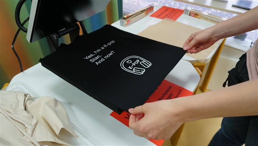 Plotter-Werkstatt für Jugendliche Ein schwarzer Stoffbeutel liegt in der Plottermaschine und ein Kind hält ihn fest