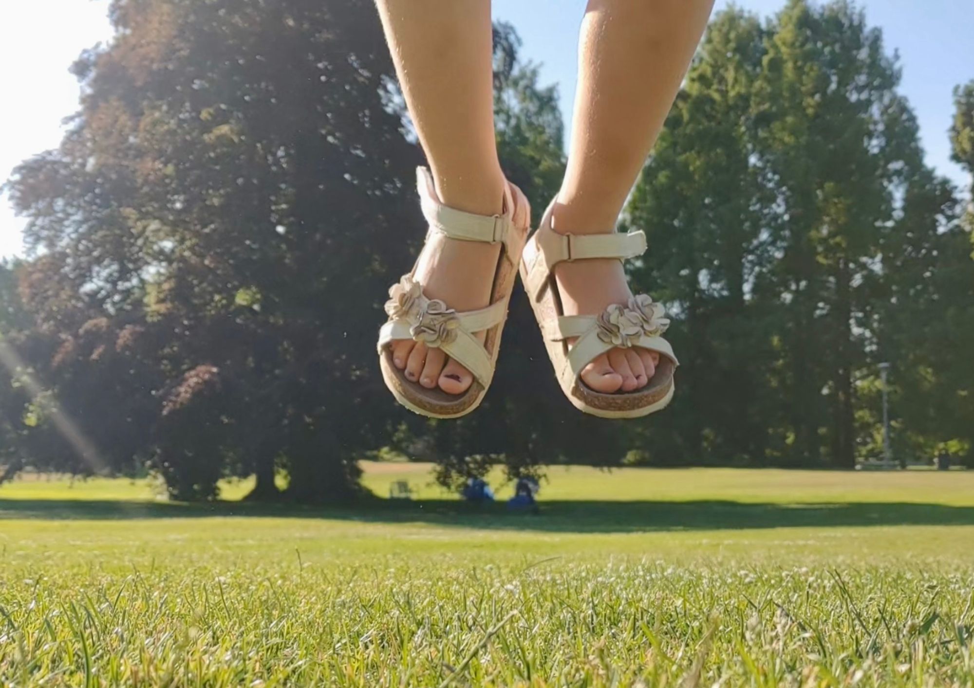 Vorleseminis im Grünen Im Hintergrund ist Wiese und Bäume zu sehen. Im Vordergrund sieht man ein paar Kinderfüße in Sandalen.