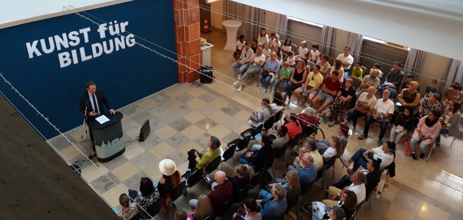 Auktion bei der Ausstellung "Kunst für Bildung". Vor zahlreichen Besucherinnen und Besuchern hält Oberbürgermeister Martin Hebich die Eröffnungsrede im Foyer des Erkenbert-Museums.