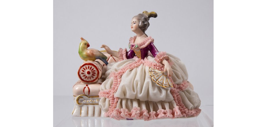 Das Objekt des Monats März 2023: Porzellanfigur der Manufaktur Friedrich Wessel, eine Dame auf einem kleinen Sessel mit einem Vogel, der auf der Lehne sitzt, darstellend.