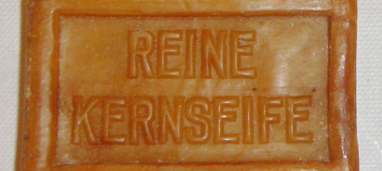 Zu sehen ein weiteres Stück Frankenthaler Kernseife, Ansicht von oben. Rechteckiges, orangebraunes Seifenstück mit dem Aufdruck "Echte Kernseife"