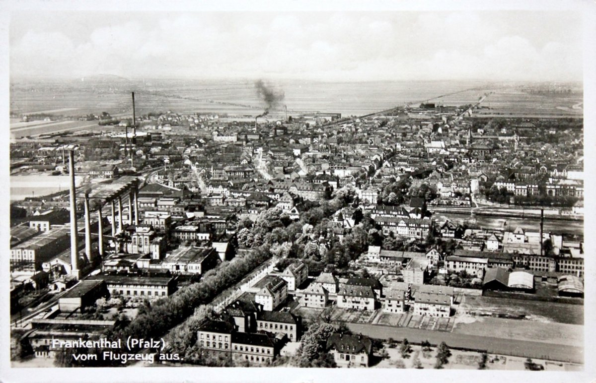 Ansichtskarte "Frankenthal (Pfalz) vom Flugzeug aus", im Vordergrund links das Gelände der Zuckerfabrik vor 1943 mit den charakteristischen sieben Schornsteinen. Quer über das Bild verlaufend von links unten bis Bildmitte die Mahlastraße mit Baumallee um die Isenach, von Südwest gesehen. Die Innenstadt beginnt etwa in der Bildmitte. Zu sehen die rauchenden Schornsteine weiterer Frankenthaler Industrie westlich der Bahnlinie. Im Hintergrund am Horizont Felder (Richtung Lambsheim und Bobenheim-Roxheim)