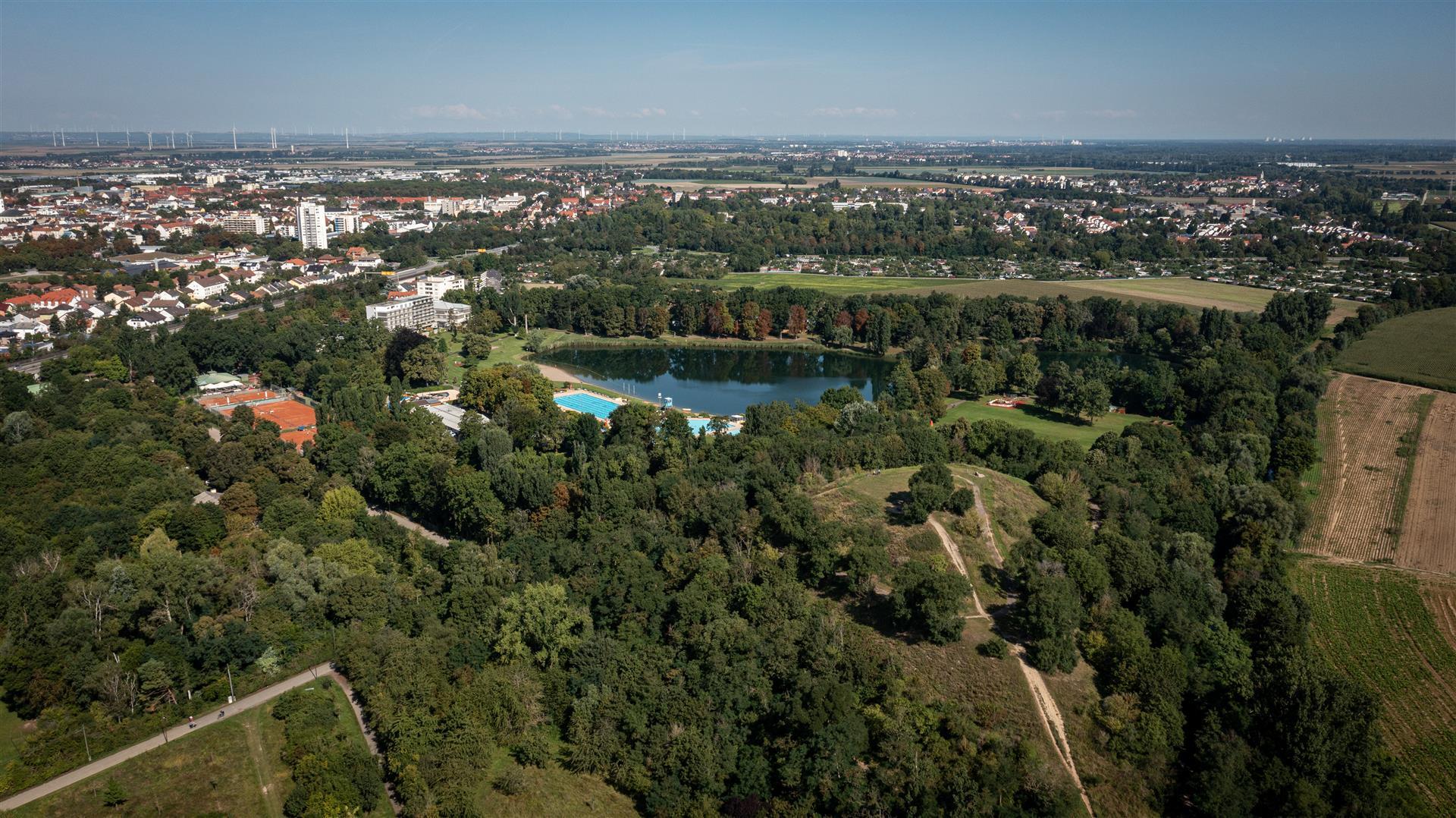 Luftaufnahme mit Wald, Schwimmbecken und Gebäuden im Hintergrund