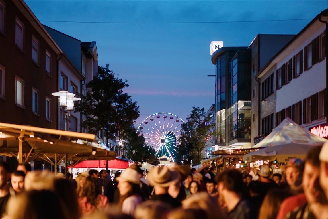 Abendstimmung bei einem Stadtfest, Menschen mit Strohhüten, Blick auf ein Riesenrad