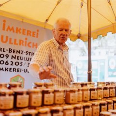 Imker Ullrich an seinem Stand, er greift nach einem Glas Honig.
