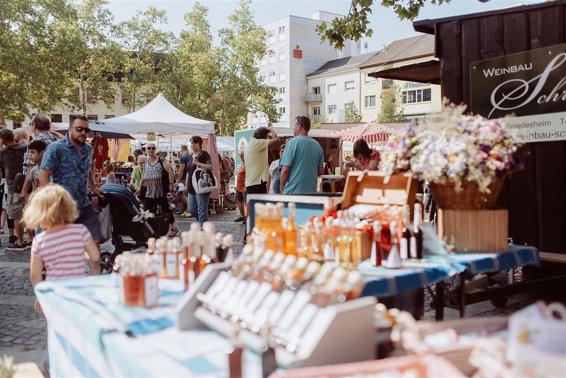 Blick auf den Rathausplatz mit Ständen und Menschen. Der Himmel ist blau. Im Vordergrund ein Marktstand.