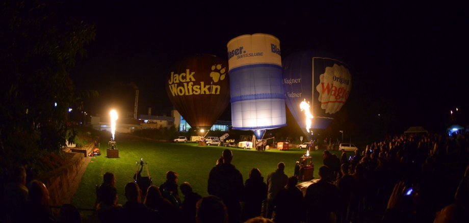 Viele Menschen im Dunkeln die glühende Heißluftballons anschauen.