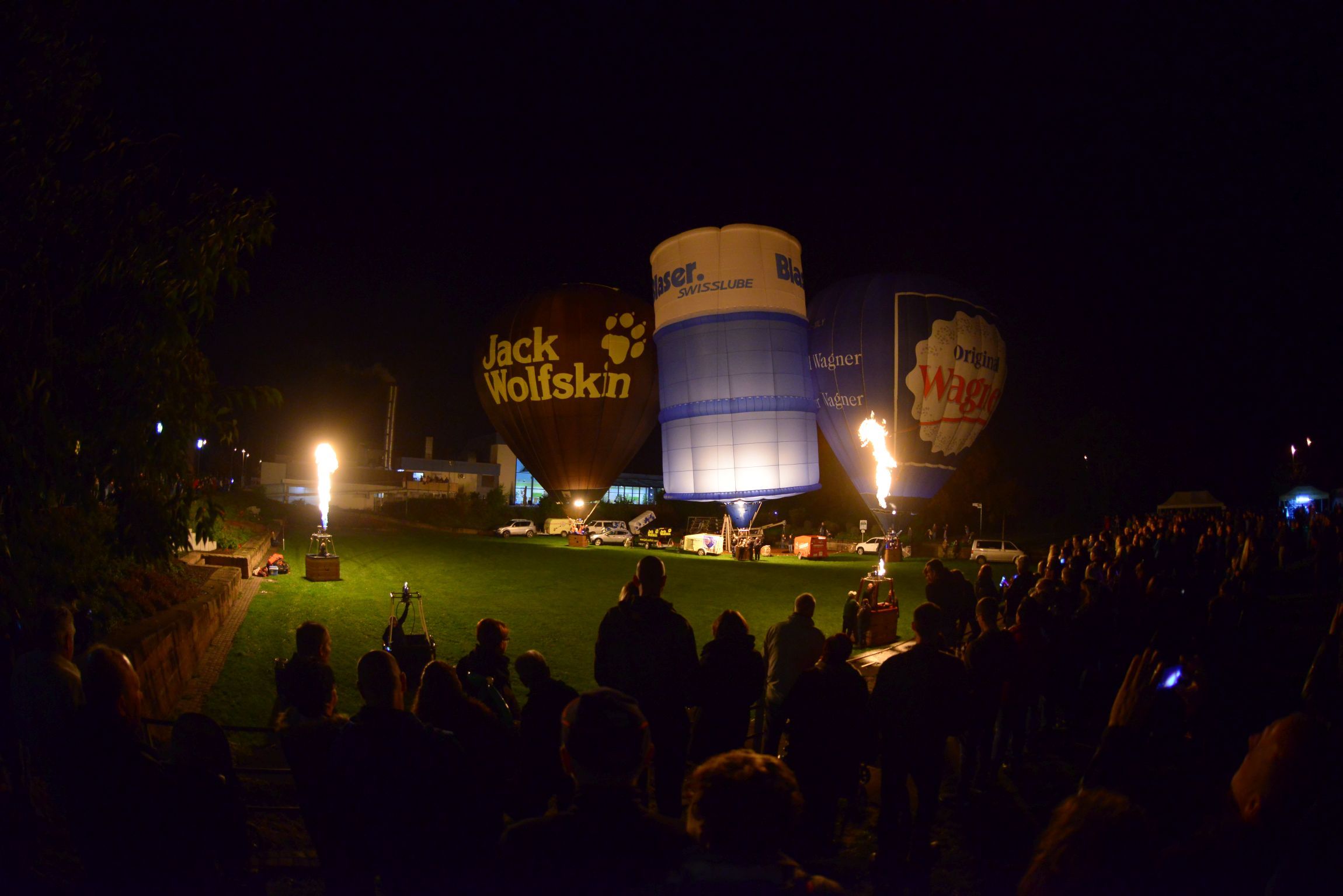Viele Menschen im Dunkeln die glühende Heißluftballons anschauen.