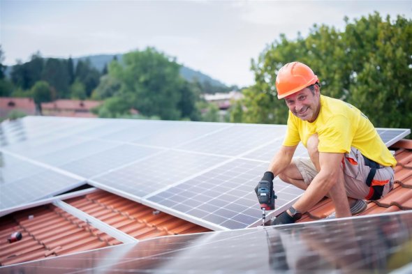 Lächelnder Arbeiter montiert eine Photovoltaikanlage auf Hausdach.
