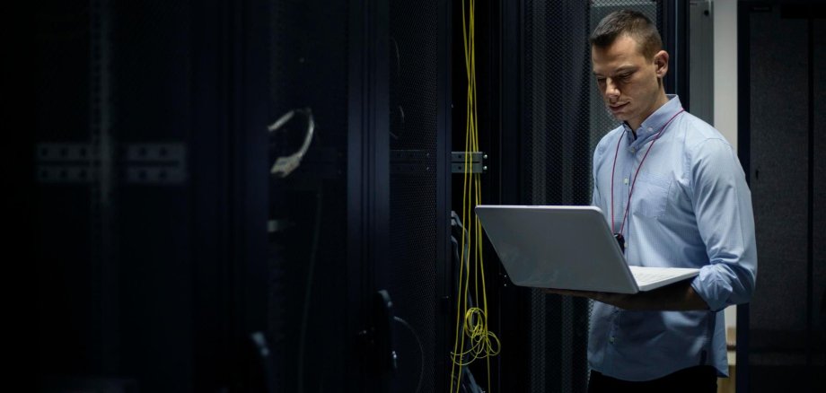 Junger Mann steht mit einem Laptop in einem Technikraum