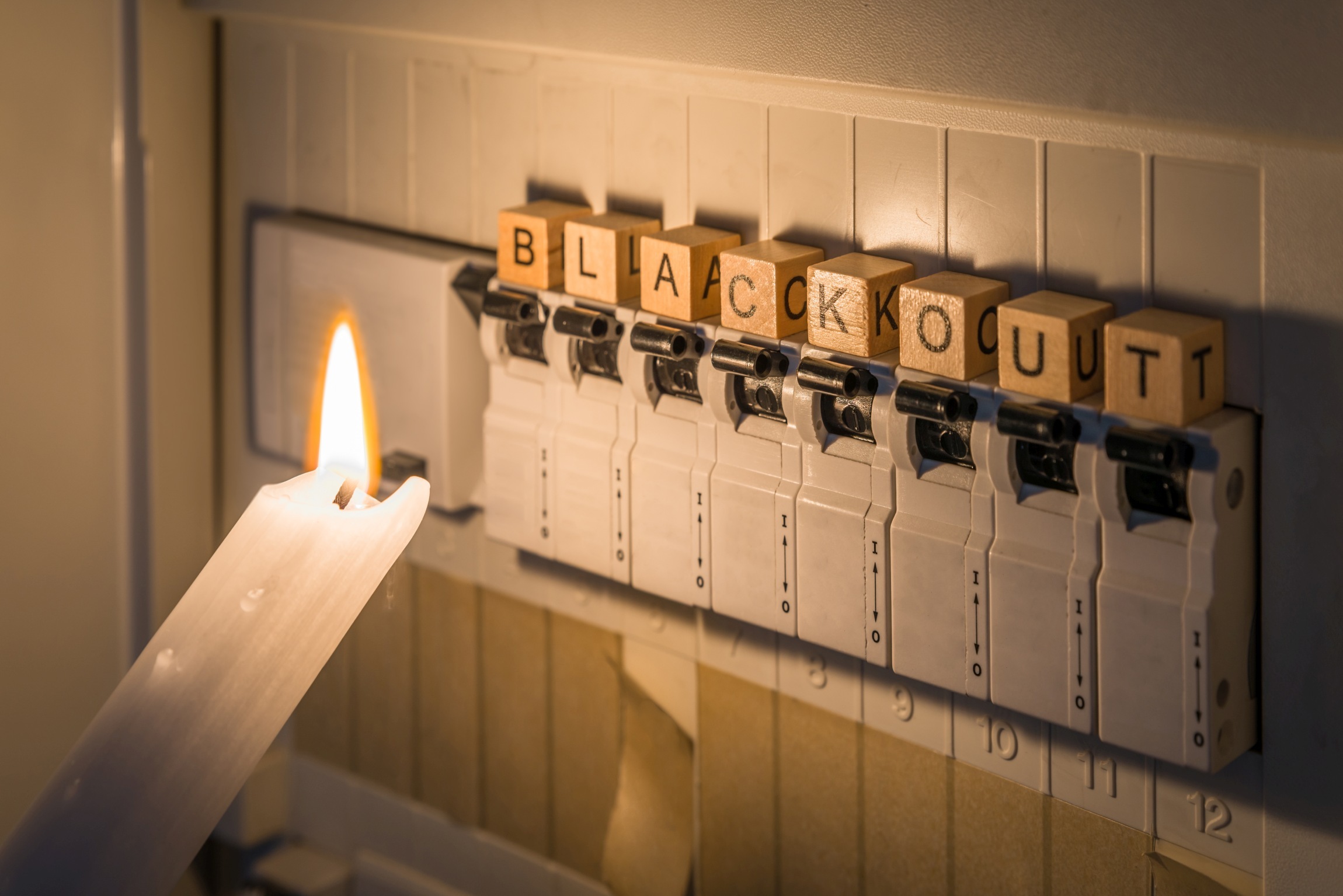 Fuse box with fuses in a distribution box during a power outage lit with white candle holding a man with the word blackout as text, Germany Stromkasten bei Stromausfall. Bild im Text: Blackout