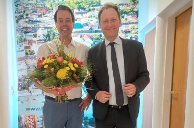 Zwei lächelnde Männer, von denen einer einen Blumenstrauß hält.