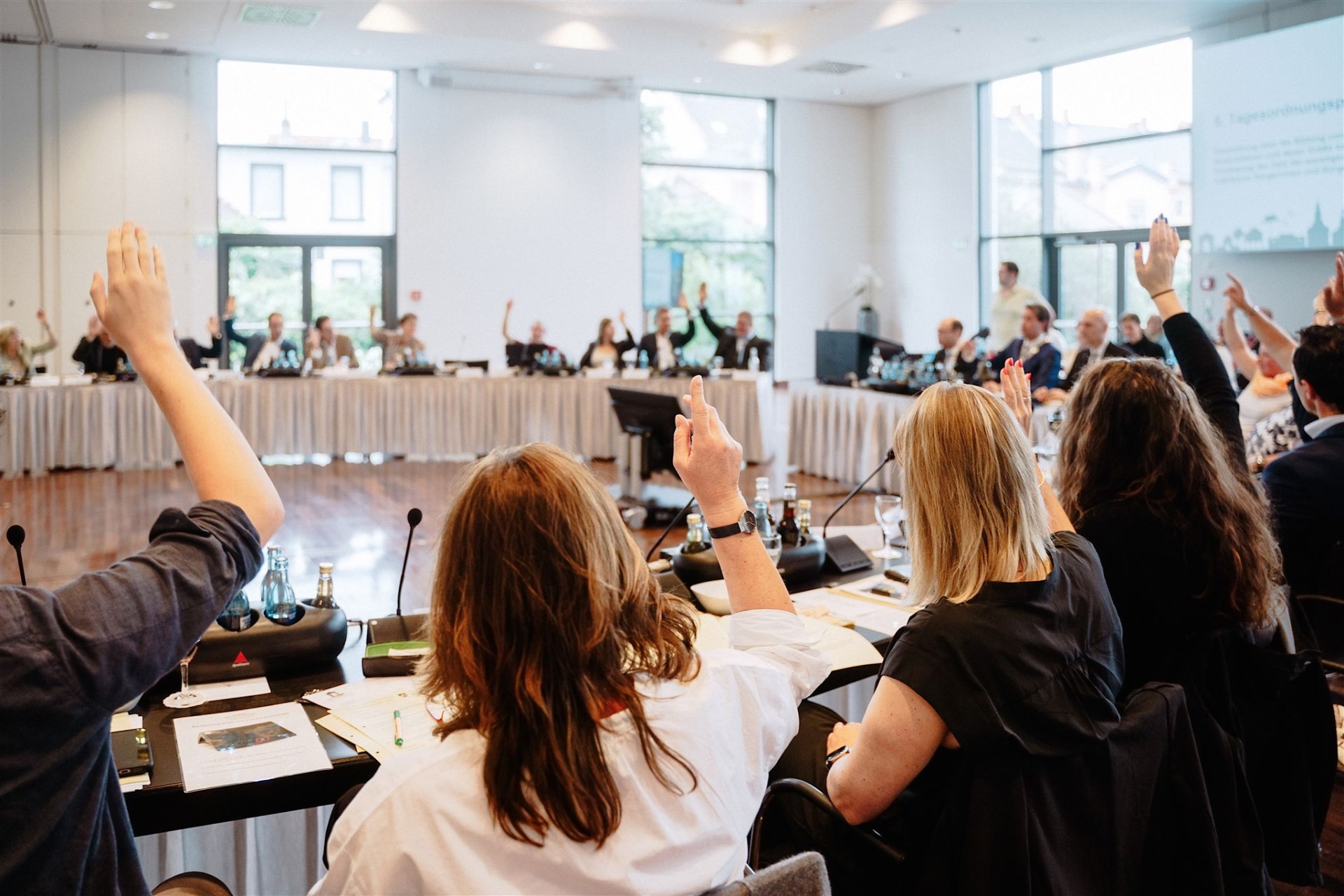 Mehrere Personen mit gehobenen Händen an einer Tischrunde