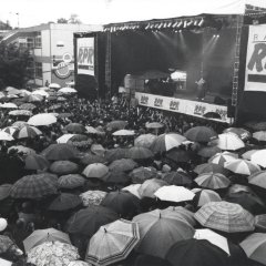 Menschenmenge mit Regenschirmen vor einer großen RPR Bühne