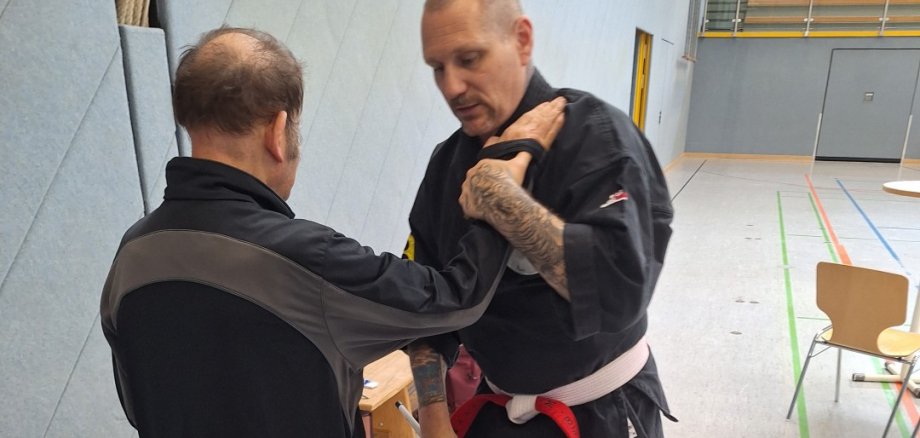 Der Trainer Marco Beyer in schwarzem Ju Jutsu Anzug hält die Hand eines der Teilnehmers.