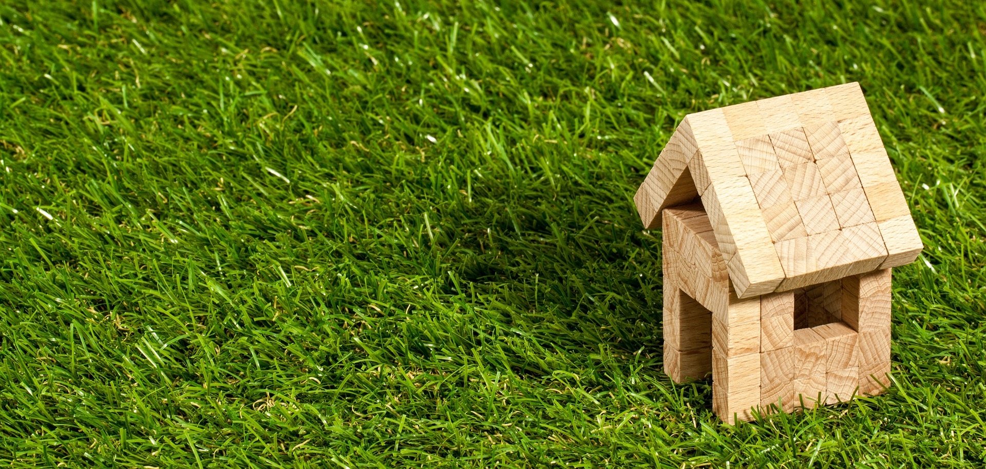 Kleines Haus aus Holzbausteinen auf grüner Wiese