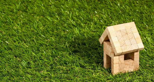 Kleines Haus aus Holzbausteinen auf grüner Wiese
