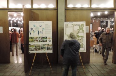 Die Analysen und Entwürfe wurden auf Plakate gedruckt und im Raum aufgestellt. Menschen schauen sich die Plakate an und sprechen über die Inhalte.