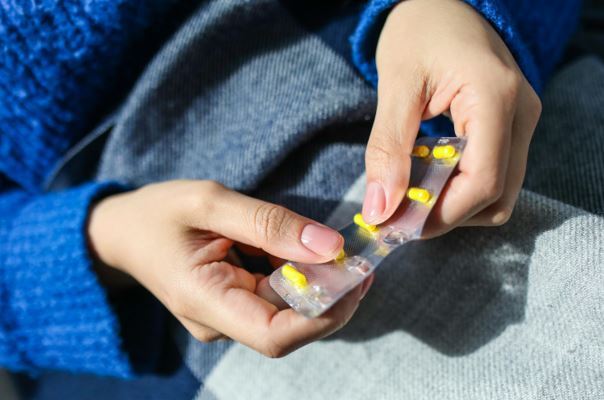Frauen - Sucht - Gewalt Auf dem Bild ist eine sitzende Frau, ab dem Bauch bis zu den Oberschenkel zu sehen. Sie hält in beiden Händen eine Anzahl von Tabletten, die noch in der Verpackung der Filmtabletten sind.