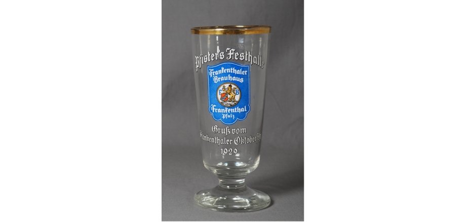 Bierglas mit der weißen Zier-Aufschrift "Pfister’s Festhalle. Gruß vom Frankenthaler Oktoberfest 1929“ und mittig dem damals aktuellen Logo des Frankenthaler Brauhauses, umgeben von der Schrift "Frankenthaler Brauhaus" (oben) und Frankenthal, Pfalz (unten) auf blauem Grund. Das Glas hat einen Goldrand. Logo des Brauhauses: Blauer Grund, mittig in Wappenform ein Löwe, der ein Wappen und einen Reichsapfel hält.