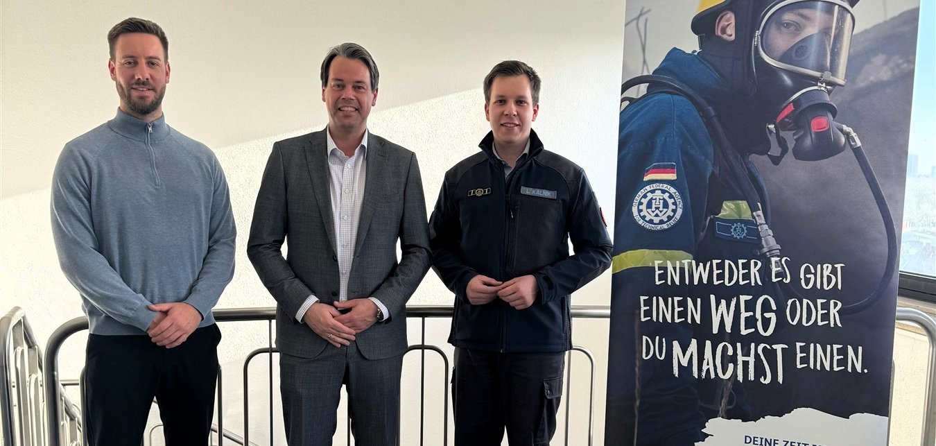 Foto von drei Herren. Einer von ihnen trägt eine dunkelblaue Uniform.