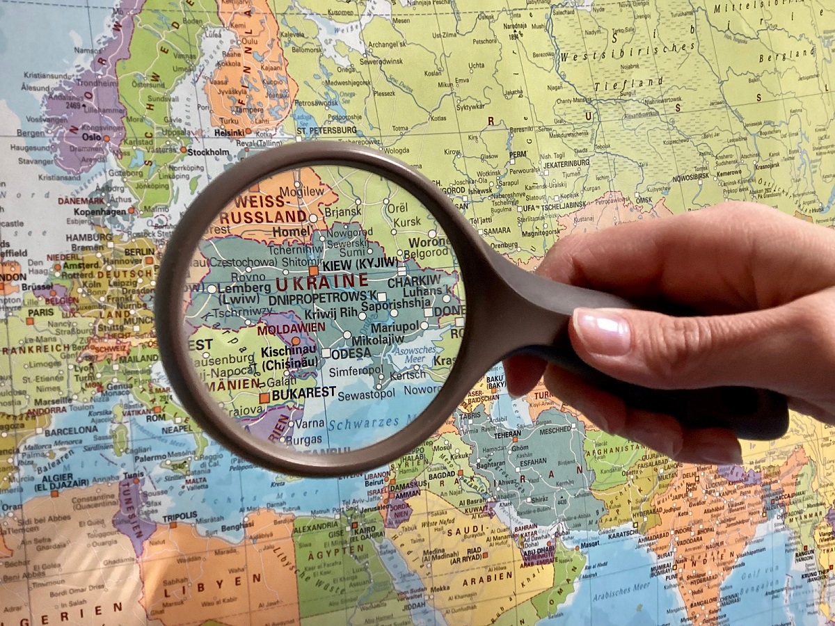 Informationen zum Krieg in der Ukraine Eine Lupe wird über eine Weltkarte gehalten, so dass das Land Ukraine vergrößert dargestellt wird.