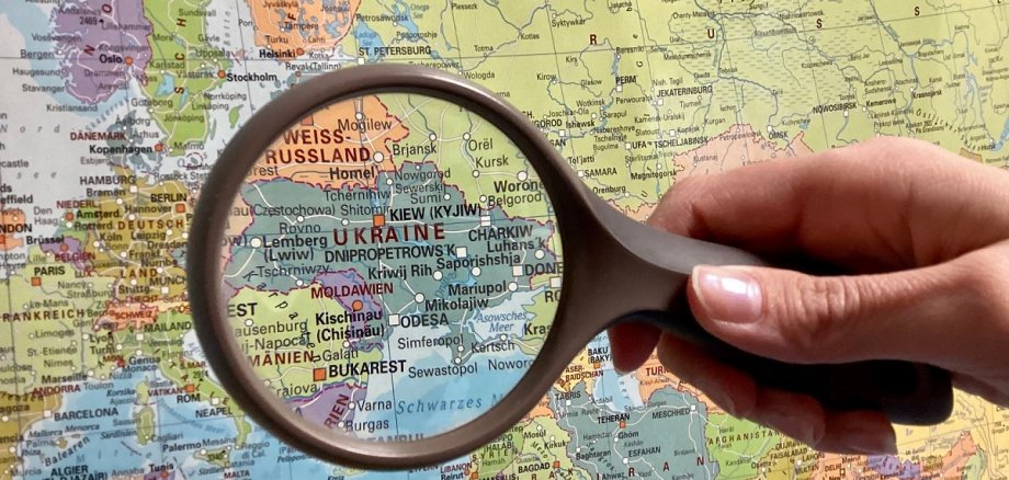 Eine Lupe wird über eine Weltkarte gehalten, so dass das Land Ukraine vergrößert dargestellt wird.