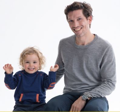Auf dem Bild ist ein Vater mit seinem kleinen Kind zu sehen, beide sehen fröhlich aus.